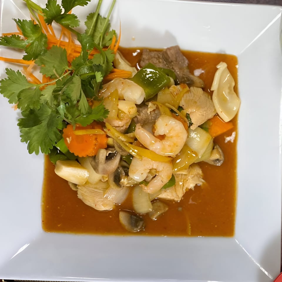 Thai stir-fry with shrimp, chicken, beef, vegetables, and sauce, garnished with cilantro and carrots.