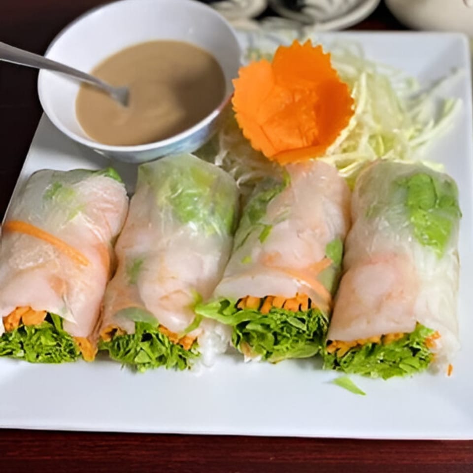 Four fresh spring rolls with shrimp, lettuce, and carrots, served with peanut sauce and shredded cabbage.
