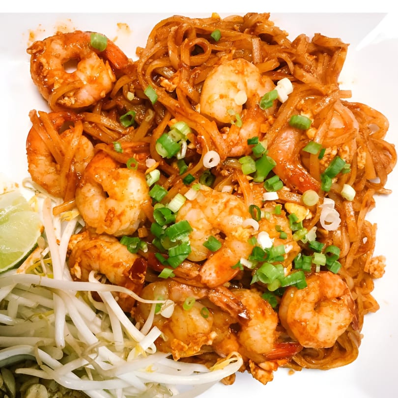 Close-up of Thai Pattaya's Pad See Ew with shrimp, bean sprouts, and lime on a white plate.